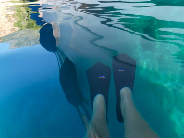 UNDERWATER sea level photo. Yacht reflection and female legs with flippers in turquoise crystal clear water off the Agia Kyriaki beach in Kyparissi Laconia village, Greece. Sea cruise summer vacation