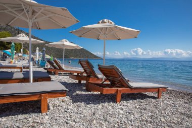 Beyaz şemsiyeler, kumlu çakıl taşlı plajlarda turkuaz kristal berrak suyla Tyros kasabası, Mora, Argolik Körfezi, Myrtoan Denizi, yaz sabahı GREECE. Yatay.