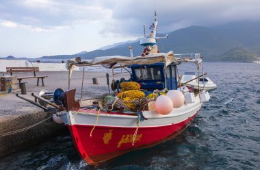 Tekne, Yunanistan 'da sakin deniz manzarası ve dağ zeminiyle çevrili olan suya hafifçe dayanıyor. Yelkenli, canlı renkler ve balıkçılık malzemeleri gösteriyor. Denizcilik maceraları için ideal..