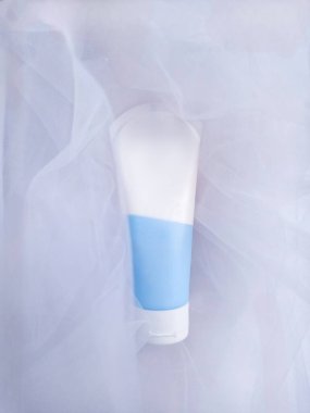 Beyaz ve mavi 75 ml plastiğin tam boy fotoğrafı beyaz kumaşın üzerinde duruyor. Güzellik kavramı, vücut bakımı. El Kremi Tüpü Paketleme.