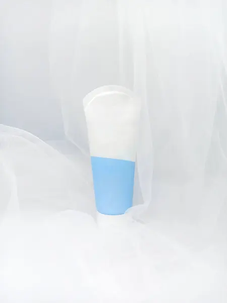 Beyaz ve mavi El Kremi 75 ml plastik tüp ambalajı beyaz şeffaf kumaş arka planda. Güzellik, dikkat konsepti.