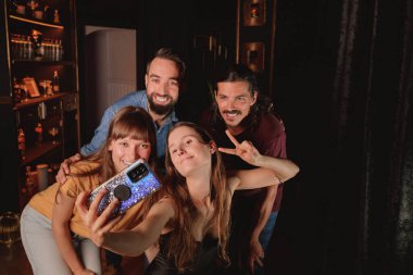 Cep telefonlu bir kız, bir gece kulübünde bir grup arkadaşıyla selfie çekiyor.
