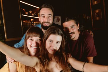 Gece kulübünde gülümseyen bir grup genç arkadaş selfie çekiyor.