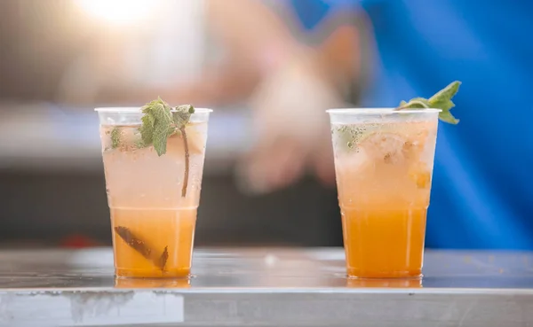 Sokak barında plastik bardaklarda renkli turuncu mojito kokteylleri. Sokak pazarında mojito 'da nane ve meyve suyu..