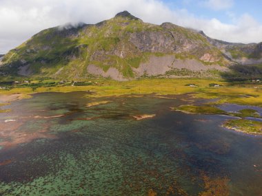 Norveç, Lofoten 'deki bir dağın manzarası, yukarıdan. Mavi gökyüzü, yamalı bulutlar ve renkli mavi deniz..