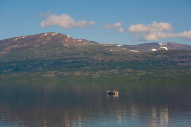 Norveç 'te Afrika' da bir tekne. Dağlar karla kaplı ve yansımalı sakin bir göl..