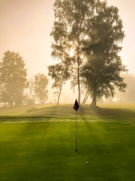 Yazın bir golf sahasında siste gün doğumu. Yeşil, bayrak ve golf topu. Mutlu ve sakin bir duygu.