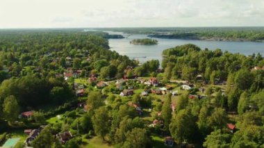 Uçurumlarda evleri olan bir köy ve İsveç takımadalarındaki ormanlarda. Güneşli bir yaz günü. Yeşil çayırlar ve yeşil ağaçlar.