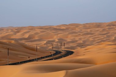 Liwa, BAE yakınlarındaki dolambaçlı çöl yolunda etrafını saran yüksek kum tepeleri var..