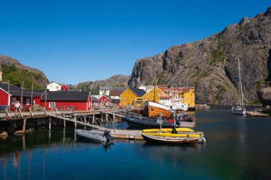 Nusfjord, Norveç - 31 Temmuz 2023: Lofoten 'in güney kıyısındaki küçük Nusfjord köyü, parlak bir yaz gününde, renkli evlerin yanında balıkçı tekneleri ve yelkenliler.
