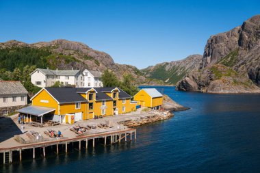 Nusfjord, Norveç - 31 Temmuz 2023: Lofoten 'in güney kıyısındaki küçük Nusfjord köyü, parlak bir yaz gününde, renkli evlerin yanında balıkçı tekneleri ve yelkenliler.