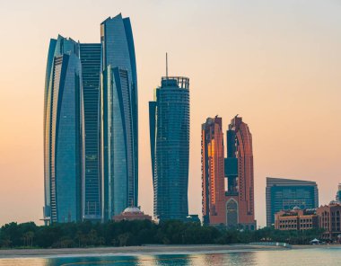 Gün doğumunda Abu Dabi 'deki Etihad kuleleri, temiz gökyüzü ve deniz yansımaları, BAE