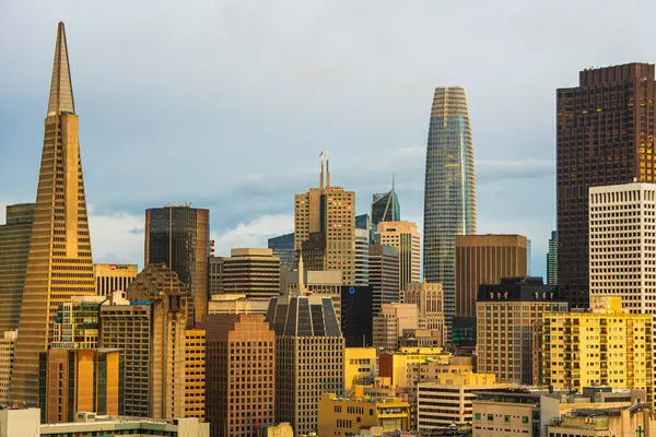 San Francisco şehir merkezindeki gökdelenler, ilkbahar yağmurundan sonra, gri gökyüzü, şehrin ufuk çizgisinde güneş ışığı. Kahverengi ve gri binalar.