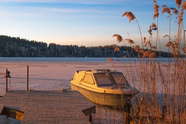 A small boat on a lake, frozen by ice and snow, in Sweden in winter. Blue sky, soft orange morning sunlight.