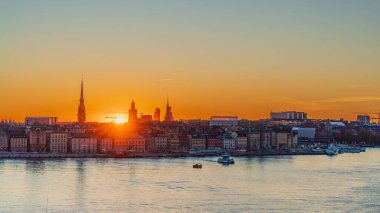 Stockholm 'de günbatımı, Gamla Stan' in ufuk çizgisi, kiliselerin silueti ve ünlü binalar. Tekne geçiyor. İsveç