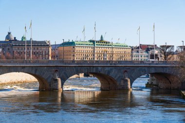 Stockholm 'le şehir merkezi arasındaki nehir. Grand Otel, İsveç bayrakları, Strombron Köprüsü. Parlak güneş ışığı, bahar. Mavi gökyüzü.