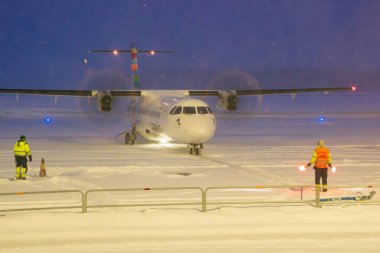 Umea, İsveç - 17 Ocak 2024: Bir ATR 72-600 uçağı Ume Havalimanı 'ndaki yoğun bir kar fırtınasında, yer personelinin rehberliğinde kendi durduğu yere taksiyle gidiyor. Yerde kar var..