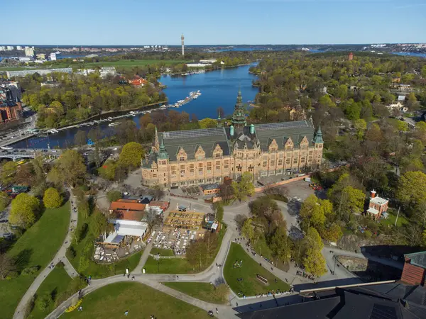 Açık bir bahar gününde İsveç 'in Stockholm kentindeki Kuzey Müzesi ve Vasa Müzesi' nin hava manzarası. Mavi gökyüzü ve yeşil ağaçlar. İnsanlar su kenarındaki parklarda dinleniyor.