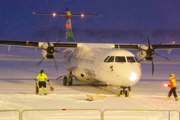 Umea, İsveç - 17 Ocak 2024: Bir ATR 72-600 uçağı Ume Havalimanı 'ndaki yoğun bir kar fırtınasında, yer personelinin rehberliğinde kendi durduğu yere taksiyle gidiyor. Yerde kar var..