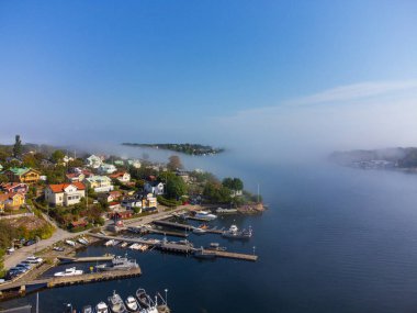 İsveç 'te, İsveç takımadası Dalaro' da sonbaharın başlarında bir adanın üzerine sabah sisi çöktü. Evler, ağaçlar, tekneler. Mavi gökyüzü, parlak güneş ışığı