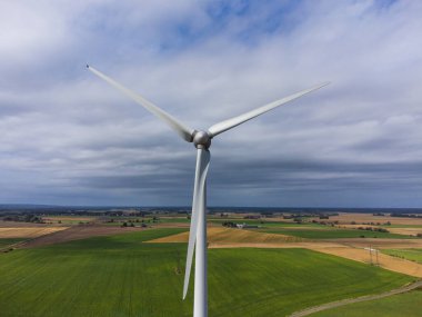 Rüzgardaki bir rüzgar türbininin hava manzarası. İsveç, yaz, yeşil ve sarı tarlalar ve tarım arazileri. Rüzgâr türbini aydınlatan güneş ışınlarıyla bulutlu.