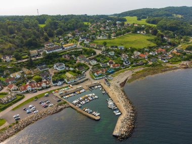 Arild, İsveç, küçük balıkçı köyü, hava manzarası, yeşil yemyeşil bitki örtüsü, renkli evler ve limandaki küçük tekneler. Puslu güneşli gökyüzü, deniz, yaz, tatil yeri.