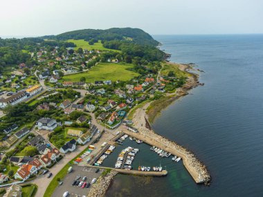 Arild, İsveç, küçük balıkçı köyü, hava manzarası, yeşil yemyeşil bitki örtüsü, renkli evler ve limandaki küçük tekneler. Puslu güneşli gökyüzü, deniz, yaz, tatil yeri.