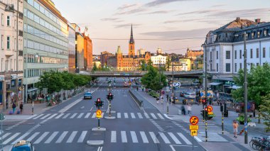 Stockholm, İsveç - 1 Ağustos 2024: Vasagatan, Vasa Caddesi, akşam ışığı, uzaktaki eski Stockholm kasabası. Turist ve yerliler cadde boyunca yürüyor, yoldan geçen arabalar.... 