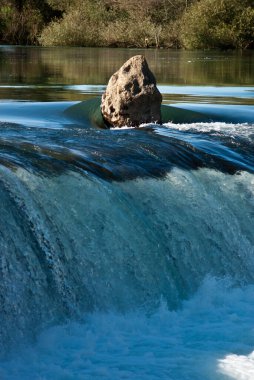 Güzel mavi bir nehirde etkileyici bir taş. Taş salın üstündeki sudan yükseliyor. Mavimsi su etrafındaki sakin bir derede akıyor..