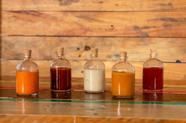 Renkli ahşap bir tabanda mantarlı el yapımı baharatlı soslar, Salsas picantes hekhas artesanalmente en botellas de vidrio con corcho sobre fondo de madera de colores