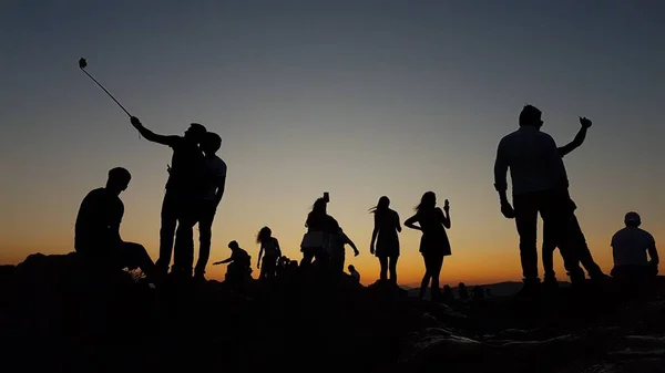 A group of diverse individuals stand united on a mountain peak, triumphant and proud, taking in the breathtaking view.