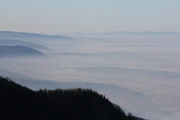 A breathtaking mountain range appears through a misty veil, with the foggy sky lending an air of mystery.