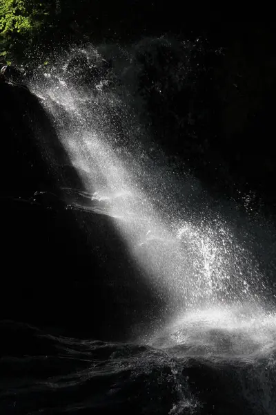 small waterfall in dark cave,where sun rays directly mixed with water