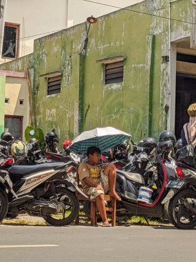Endonezya 'da. Surakarta 07 Aralık 2023. Motosiklet parkında elinde şemsiyeyle nöbet tutan küçük bir çocuk.