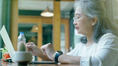 Aktif kıdemli emekli Asyalı iş kadını, güneşli bir günde kendi online küçük işletmesinde çalışmayı ve kahvecide dinlenmeyi seviyor.