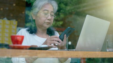 Aktif kıdemli emekli Asyalı iş kadını, güneşli bir günde kendi online küçük işletmesinde çalışmayı ve kahvecide dinlenmeyi seviyor. 