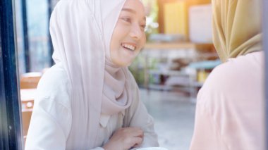 Genç ve güzel Asyalı Müslüman kadınlar güneşli bir günde kafede cep telefonuyla oynayıp dinleniyorlar. 