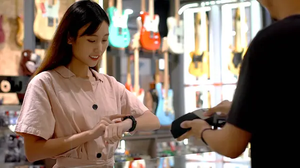 Young Asian woman using smartwatch to purchase product at the point of sale terminal in a retail store with near field communication nfc radio frequency identification payment technology
