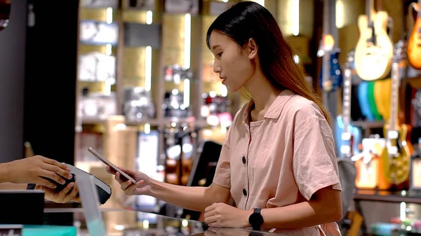Young Asian woman using smartwatch to purchase product at the point of sale terminal in a retail store with near field communication nfc radio frequency identification payment technology