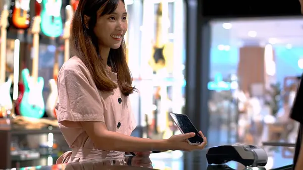 Young Asian woman using mobile phone to purchase product at the point of sale terminal in a retail store with near field communication nfc radio frequency identification payment technology