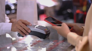 Cep telefonu kullanan üst düzey bir Asyalı Müslüman kadın. NFC kimlik doğrulama ve kimlik doğrulama ödemesi ile birlikte bir satış terminalinde ürün almak için ukalalık yapıyor.