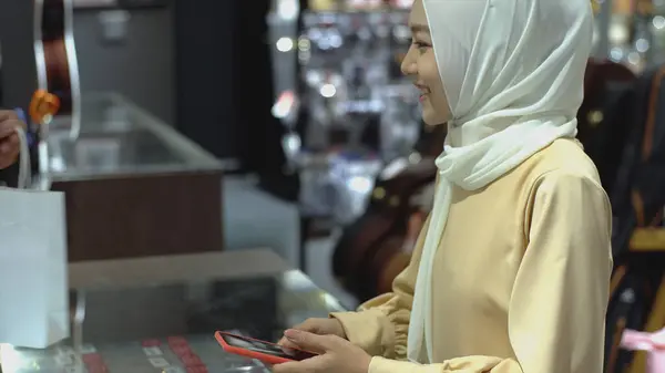 検証と認証のためのNfc身分証明の支払いを有する販売端末で製品の支払いに携帯電話を使用して上向きのモバイルアジアのムスリム女性 — ストック写真