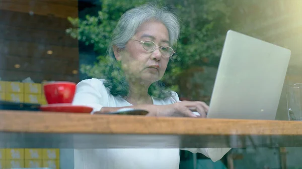 Active senior retired Asian business woman enjoy working on her own online small business and relaxing in a coffeeshop on a bright sunny day