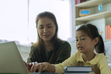 Güzel bir Asyalı anne çocuklarına evde dizüstü bilgisayarla bakıp öğretmekle meşgul.