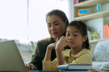 Güzel bir Asyalı anne, çocuğuna evde dizüstü bilgisayarla bakıp öğretmekle meşgul.