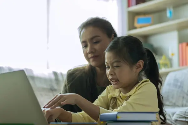 A Beautiful Asian mother busy working while looking after and teaching her child on a laptop computer at home