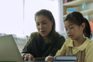 Güzel bir Asyalı anne, çocuğuna evde dizüstü bilgisayarla bakıp öğretmekle meşgul.