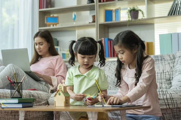 Güzel bir Asyalı anne çocuklarına evde dizüstü bilgisayarla bakıp öğretmekle meşgul.