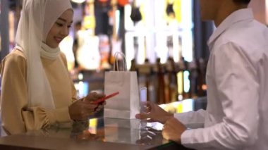 Cep telefonu kullanan üst düzey bir Asyalı Müslüman kadın. NFC kimlik doğrulama ve kimlik doğrulama ödemesi ile birlikte bir satış terminalinde ürün almak için ukalalık yapıyor. 