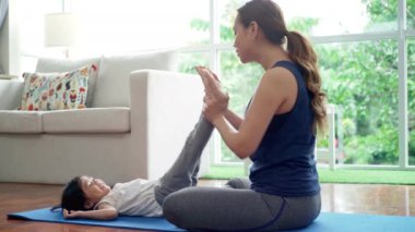 Asyalı bir anne, kızıyla yoga egzersizleri öğretir ve pratik yapar. Yoga minderleri üzerinde. Parlak, güneşli sabah oturma odalarında. 